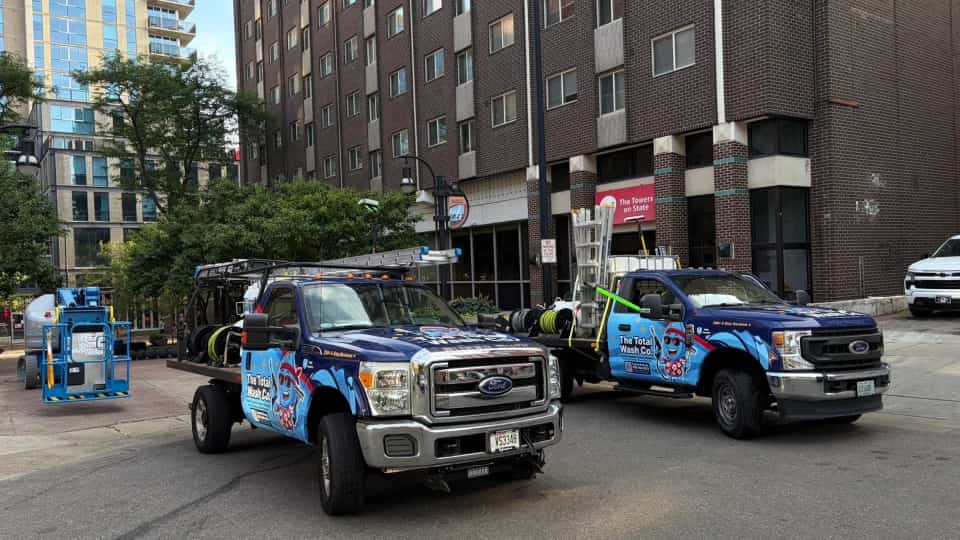 Two fully-wrapped The Total Wash Co. trucks and a boom lift staged below high-rise apartment towers in downtown Madison, WI